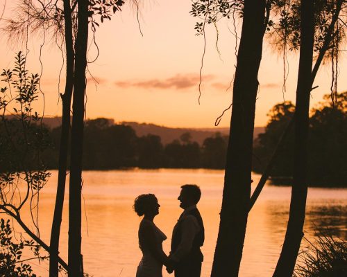 Bride and groom silhouetted by the river at sunset at The Rocks Yandina